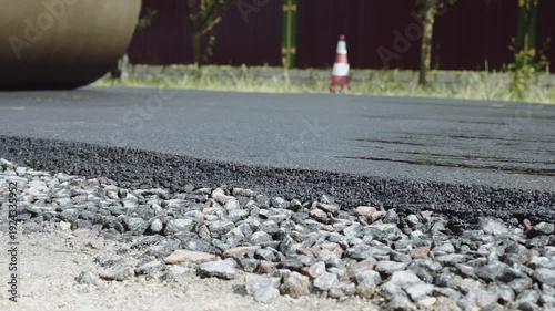 A road roller levels and compacts fresh asphalt as construction machinery builds a new road in a small town. Workers repair and smooth the surface, supporting city growth and infrastructure developmen