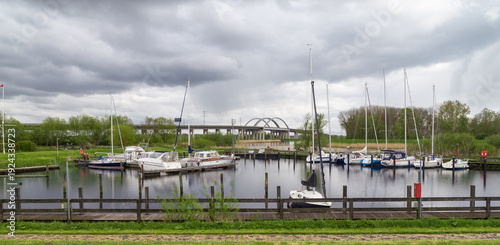 Stormy sky above a quiet marina with sailboats and reflections on the shore. In the background, a highway bridge over the Stör River. Itzehoe. Germany.