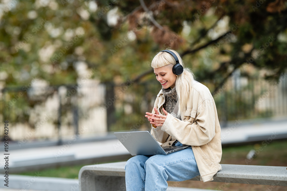 Obraz premium Woman having video call in park with laptop and headphones