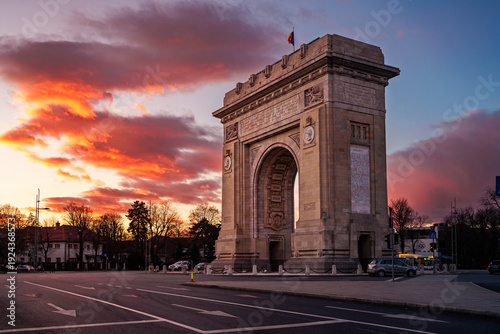 Arcul de Triumf (Arc de triomphe) in Bucharest at sunset, illuminated by warm evening light under dramatic clouds, a historic monument and national landmark in Romania’s capital city.