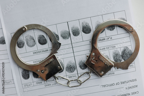 Handcuffs and fingerprints card on the white table. Crime investigation concept.