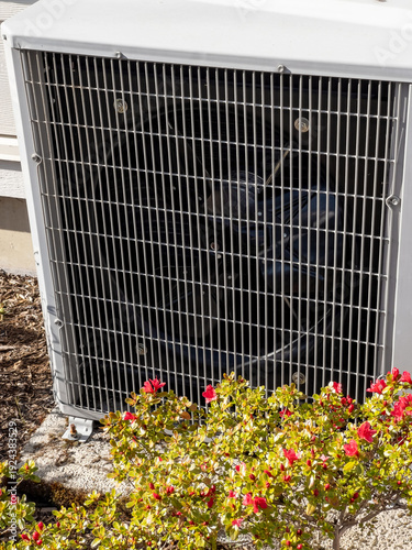 The outdoor unit of a central heating system for a home with colorful flowers in the sun