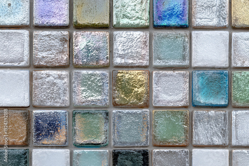 A close up view of a mosaic tile wall with an iridescent shimmering effect in various colors including blue green gold and purple