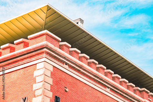 Modern architectural design meets historic brick building with crenellated parapet under blue sky