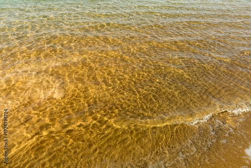 The gentle waves of the sea, rippling against the sandy shore, are illuminated by the warm rays of the summer sun
