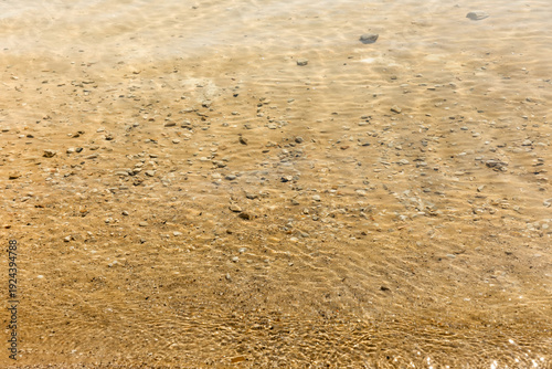 The gentle waves of the sea, rippling against the sandy shore, are illuminated by the warm rays of the summer sun