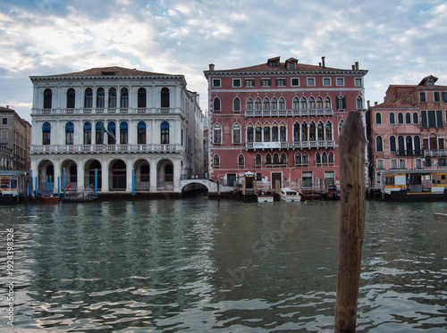 Schilderij op canvas Venice Grand Canal Palazzo Facades View - Wide view of historic Venetian palaces on the Grand Canal waterfront with a mooring post in the foreground and a rippling water texture under a cloudy sky
