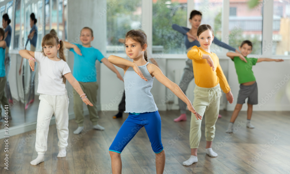 Obraz premium Active preteen girl practicing sport dances with other children and teacher during dancing classes