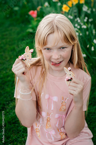 Playful blonde girl holding bunny shaped cookies in garden