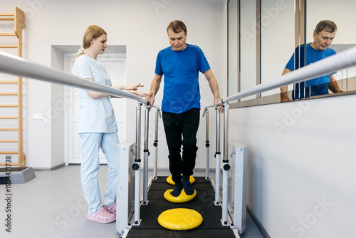 Foto Male patient performing balance exercises on a stability platform with assistanc