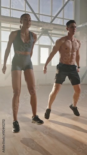 Determined athletic young man and woman doing jumping jack or jumping squats indoors. Slow motion
