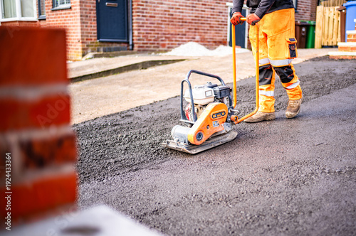 Construction workers preparing for asphalt works wearing hi vis using tools and machines to level ground and compact the area workers with wheel barrows 