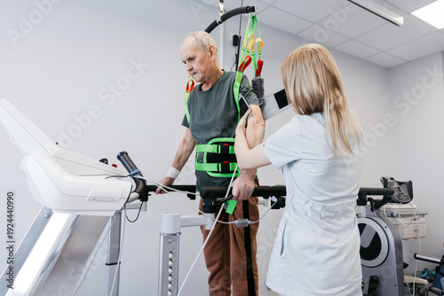 Obraz na plátně Elderly male patient undergoing robotic gait training with assistance from a fem