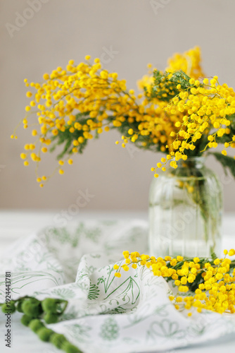 Spring still life with mimosa bouquet in glass jar on table with decorative fabric