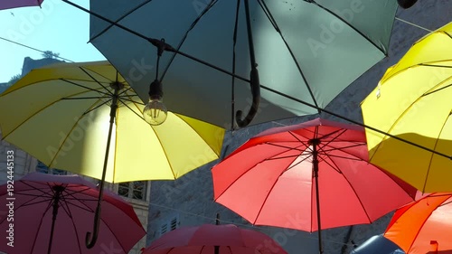 Colorful umbrellas hanging in a street art installation. Multicolored umbrellas floating against a bright blue sky, creating a vibrant and cheerful street decoration on a sunny summer day