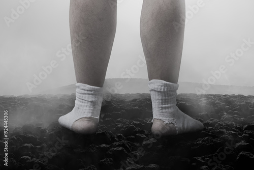 Digital composition of male feet stand on hot lava rocks with torn socks