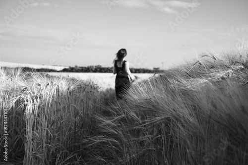 Dramatic black and white shot of a woman in a dark dress running through a tall grain field towards the horizon, symbolizing freedom, solitude, and artistic mystery