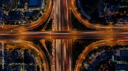 Aerial view of a glowing highway interchange at night, surrounded by buildings