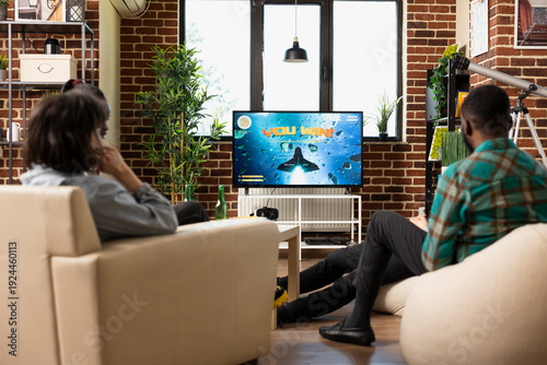 Foto Male and female friends sit around television displaying you win message during gaming hangout at home