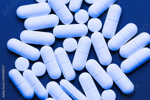 Фотография White medical tablets scattered on blue surface