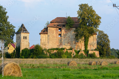 Abandoned historic brick castle ruins overgrown with trees and round hay bales in a rural summer field