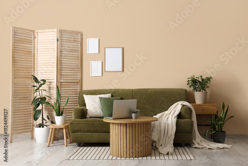 Interior of cozy living room with green sofa, folding screen and plants