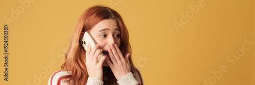 Foto Happy red-haired woman dressed in sweater, talking on mobile phone, receiving good news, winning on yellow background