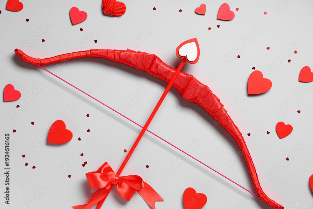 Naklejka premium Composition with red cupid's bow and paper hearts on grey background. Valentine's Day celebration