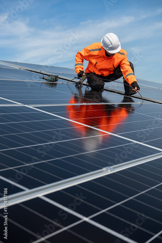 Technician installing solar panels on factory roof for green energy. A skilled technician in safety gear is working on a solar panel installation on rooftop.