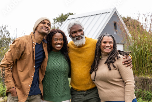 Quadro su tela Diverse friends hugging in yard in front of small shed, wearing knit sweaters an