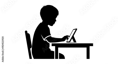Silhouette of little boy sitting at desk using tablet computer for online education or games
