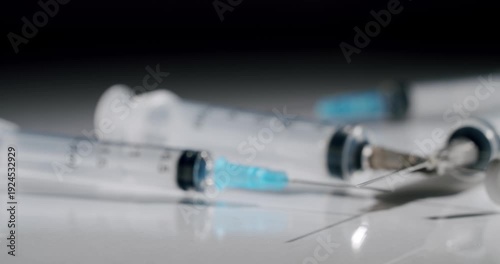 Empty plastic medical syringes with sharp needles lying on a reflective white surface against a dark background, representing healthcare, vaccination, or medical procedures