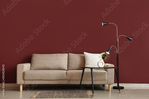 Interior of stylish living room with cozy grey sofa, coffee table and standard lamp near red wall