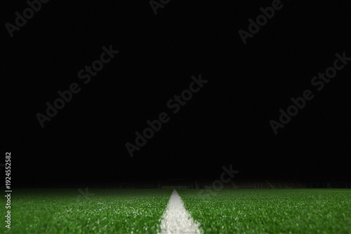 Soccer field turf at night featuring a white sideline leading into a dark background with ample copy space. This low-angle close-up of a professional football pitch at Sciorba Stadium captures themes 