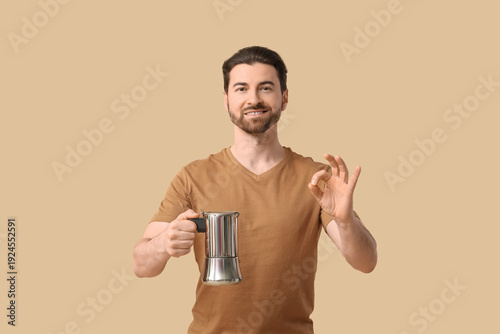 Young man with geyser coffee maker showing OK gesture on beige background