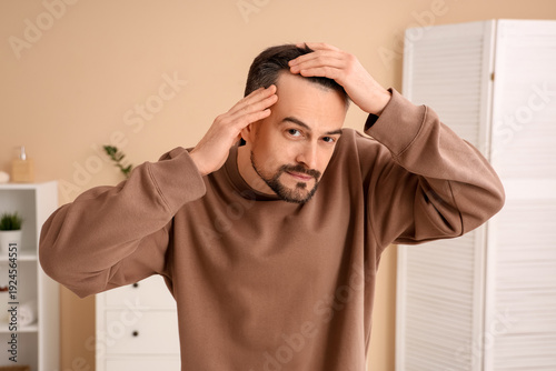 Handsome man with hair loss problem in bathroom