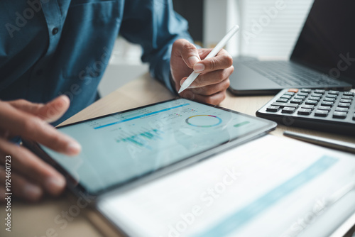 Business professional analyzing financial data on digital tablet dashboard with calculator and laptop, representing accounting software, ERP system integration, performance monitoring.