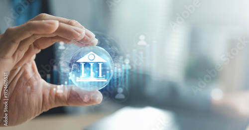Quadro su tela Hand holding digital bank icon with financial data interface, concept of online banking service, secure money transfer and financial technology in global economy