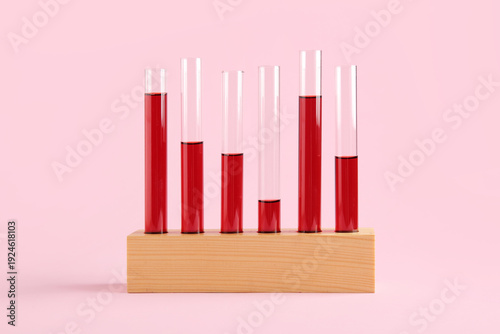 Test tubes with samples in wooden stand on pink background