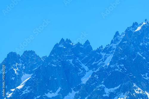 Картината върху платно Rugged, jagged summits of Aiguille de Blaitiere rise sharply against a vivid blue sky, with patches of lingering snow accentuating the dramatic alpine rock formations