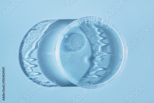 Slika na platnu Petri dish holding clear liquid casting rippling shadows on blue background