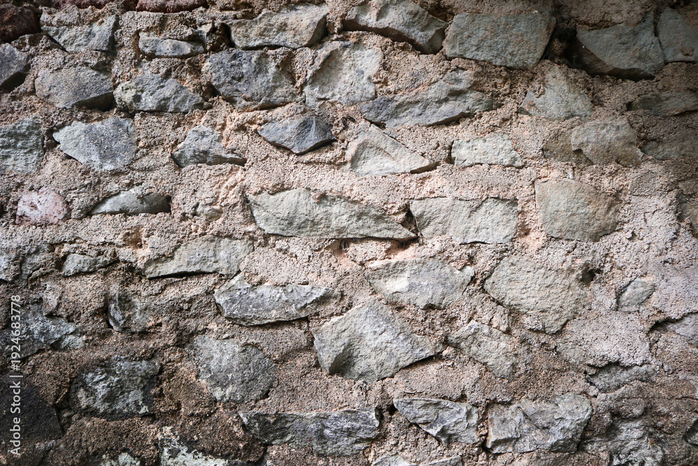 Fototapeta premium Close-up of a rugged retaining wall built from irregular grey stones embedded in a coarse, sandy beige mortar, showing natural geological textures.