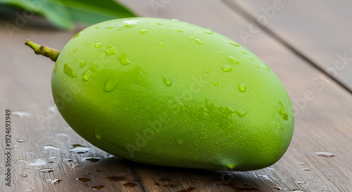 A close-up shot of a single, dew-kissed unripe green mango resting on a rustic wooden surface, showcasing its smooth skin and freshness