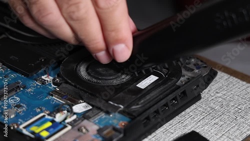 Close up of technician servicing dusty laptop cooling fan during computer maintenance and repair work improving airflow and device performance