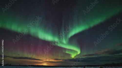 A stunning display of the Aurora Borealis (Northern Lights) over a winter landscape. Bright, twisting green lights dominate the starry night sky, blending with hints of purple and pink below.