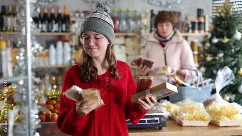 Adolescence girl customer choose nougat, aunt companion in background with shop basket trolley- national European sweet desserts in sales area. 