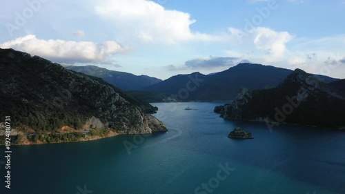 Scenic drone view of Lac de Castillon surrounded by rugged mountains and clear blue water in the French Alps under a partly cloudy sky.