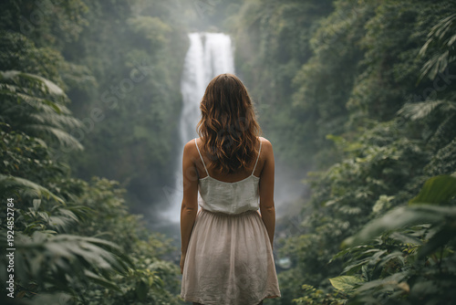 A woman stands before the cascading waterfall, immersed in the beauty of nature. The verdant scenery evokes tranquility.  