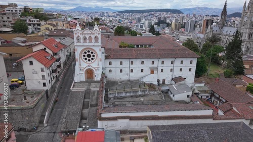 Aerial side view of Monastery of The Incarnation of St. John showing central staircase, courtyard, pedestrian and city skyline with Andean mountains in background.