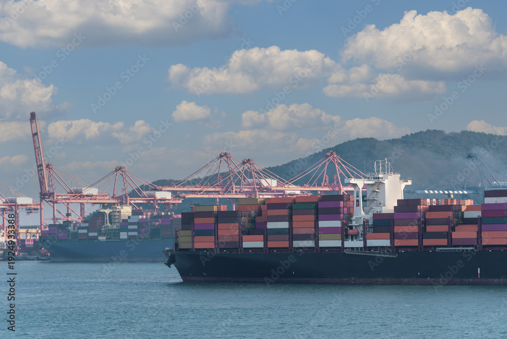 Fototapeta premium A large cargo ship loaded with colorful shipping containers approaches a container terminal in Busan, South Korea. Symbolizing efficiency in global maritime commerce. 